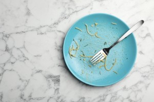 Dirty plate with food leftovers and fork on marble background, top view. Space for text